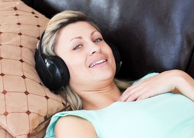 Uśmiechnięta kobieta kłama na kanapie i słucha muzykę
