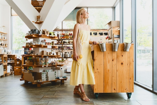 Uśmiechnięta kobieta kupuje żywność ekologiczną i produkty ekologiczne w zrównoważonym sklepie bez plastiku