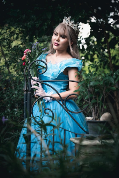Uśmiechnięta kobieta nosząca koronę patrząca w inną stronę, stojąc przed roślinami