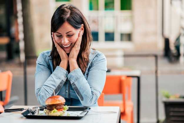 Uśmiechnięta kobieta patrzeje hamburger w outdoors restauraci.