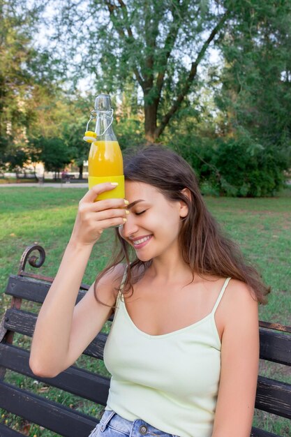 Zdjęcie uśmiechnięta kobieta pijąca sok siedząc w parku publicznym