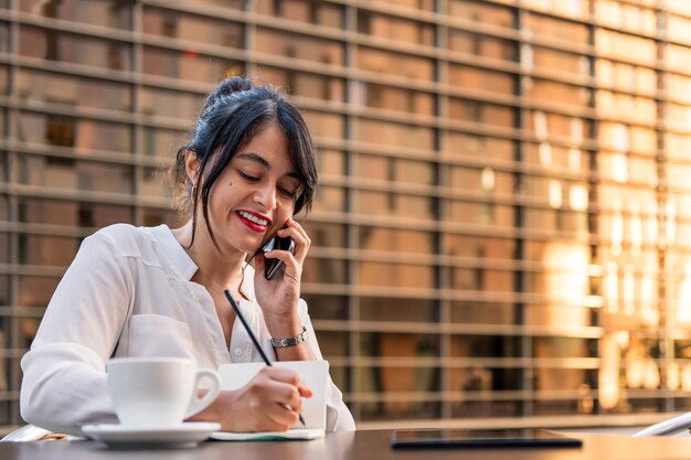 Uśmiechnięta kobieta pracuje i rozmawia przez telefon na tarasie kawiarni, koncepcja cyfrowego przedsiębiorcy i miejskiego stylu życia, skopiuj miejsce na tekst