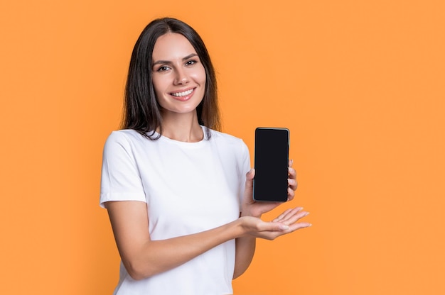 Uśmiechnięta kobieta prezentująca urządzenie mobilne Technologia mobilna Komunikacja mobilna Prezentowanie przestrzeni kopiowania produktu Szczęśliwa kobieta prezentującą telefon komórkowy