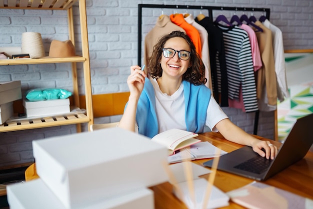 Uśmiechnięta kobieta robi notatki z zamówień z laptopa Właściciel Dropshipping pracuje