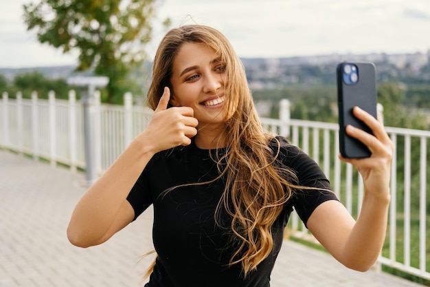 Uśmiechnięta kobieta robi selfie swoim telefonem, podczas gdy wiatr wieje jej włosy