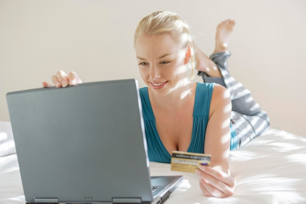 Zdjęcie uśmiechnięta kobieta robi zakupy online za pomocą laptopa w łóżku w domu