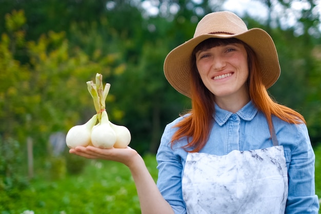 Uśmiechnięta Kobieta Rolnik Ogrodnik Trzyma W Ręku świeżo Wykopaną Roślinę Czosnku