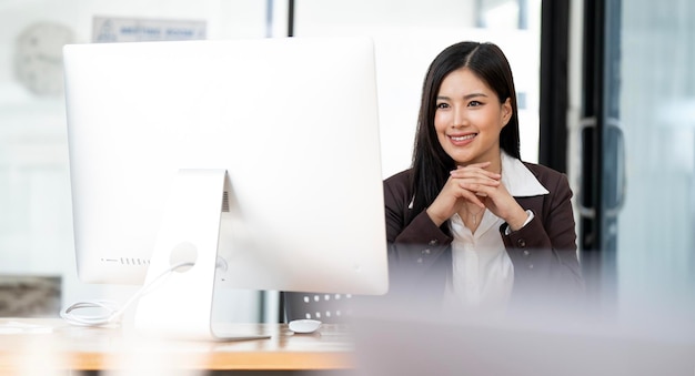 Uśmiechnięta kobieta siedząca przy biurku w biurze szczęśliwa kobieta biznesowa siedząca w biurze z rękami dotykającymi jej podbródka