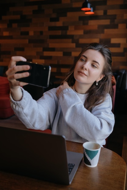Uśmiechnięta kobieta siedzi na kuchennej sofie rozmawiając przez wideorozmowę randkową online, patrząc na telefon