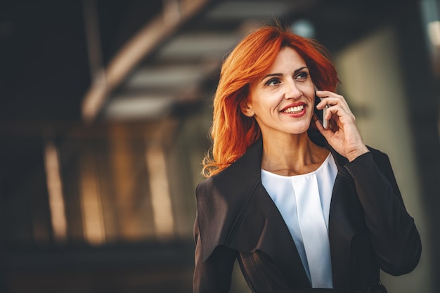 Zdjęcie uśmiechnięta kobieta sukcesu w biznesie rozmawia na smartfonie w dzielnicy biurowej.