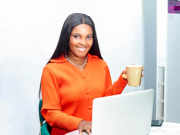 Uśmiechnięta kobieta surfująca po sieci na laptopie podczas picia kawy w swoim biurze