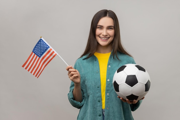 Uśmiechnięta kobieta trzyma flagę USA i czarno-białą piłkę zjednoczonej ligi piłki nożnej