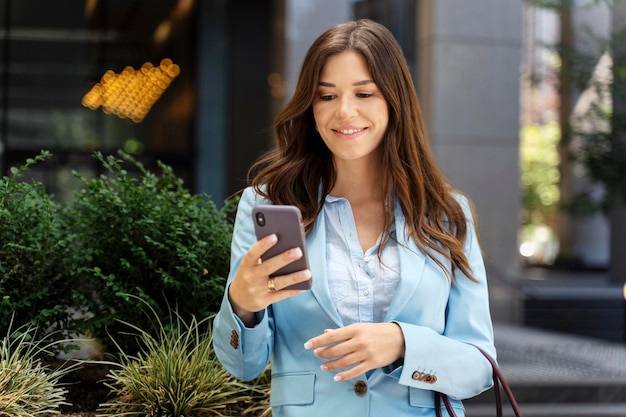Uśmiechnięta kobieta trzymająca telefon komórkowy, robiąca zakupy online, czytająca wiadomości tekstowe, oglądająca filmy w biurze.