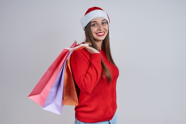 Uśmiechnięta kobieta ubrana w santa hat, czerwony sweter, trzymając torby na zakupy. Koncepcja świątecznych wyprzedaży, zakupów, rabatów.