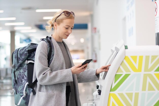 Uśmiechnięta kobieta używająca smartfonu, stojąca przy bankomacie