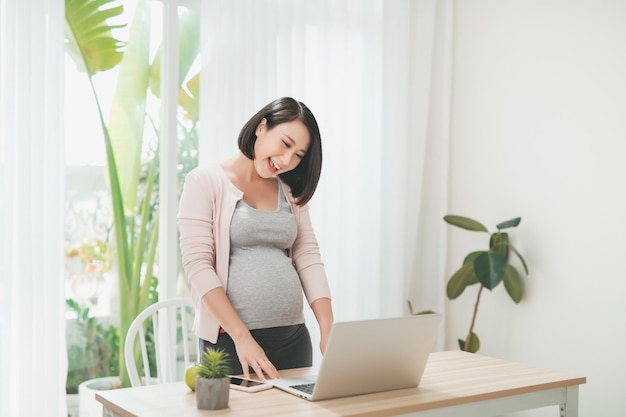 Uśmiechnięta kobieta w ciąży korzysta z laptopa w domu Zakupy online koncepcja ciąży na kopii przestrzeni