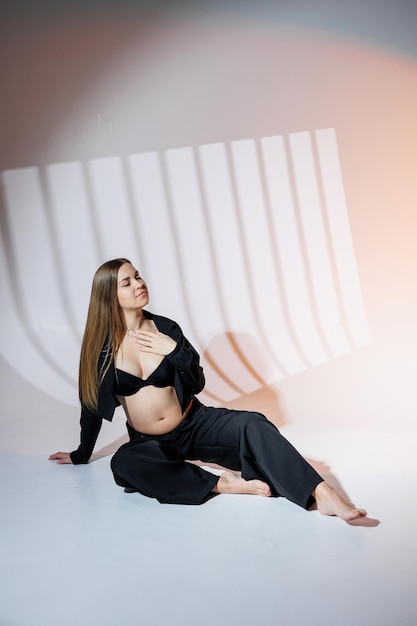 Uśmiechnięta kobieta w ciąży w czarnym garniturze na szarym tle Piękna elegancka kobieta w ciąży