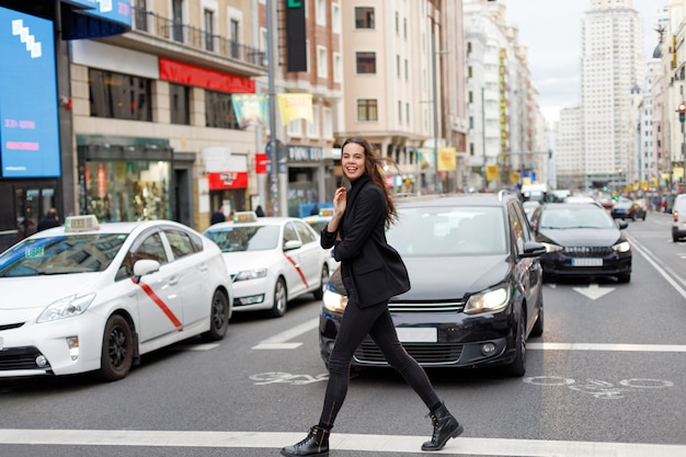 Uśmiechnięta kobieta w czarnej kurtce przekraczania ulicy w centrum miasta