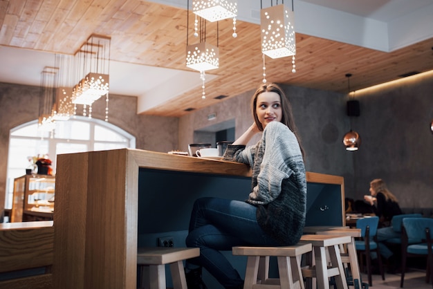 Uśmiechnięta kobieta w kawiarni przy użyciu telefonu komórkowego i SMS-y w sieciach społecznościowych, siedząc samotnie