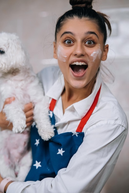 Uśmiechnięta kobieta w kuchni trzymająca słodkiego białego maltańskiego psa