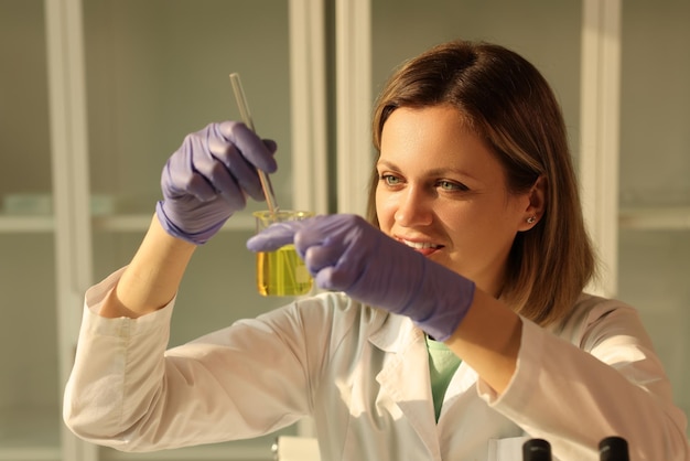 Zdjęcie uśmiechnięta kobieta w laboratorium z tubką z żółtym płynem odczynnikiem chemicznym do zbliżenia