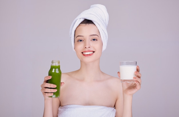 Uśmiechnięta kobieta w ręczniku trzyma szklankę mleka i butelkę z smoothie.