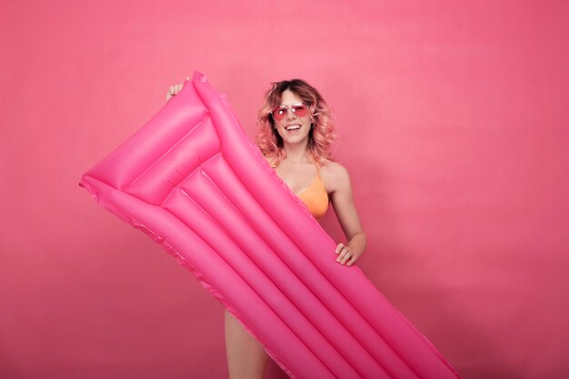 Uśmiechnięta kobieta w stroju kąpielowym z nadmuchiwanymi noszami basenowymi na różowym tle