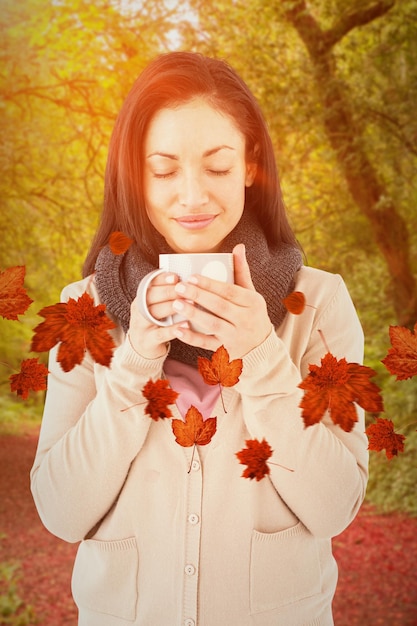 Uśmiechnięta kobieta wącha gorący napój przed pokojową jesienną sceną w lesie