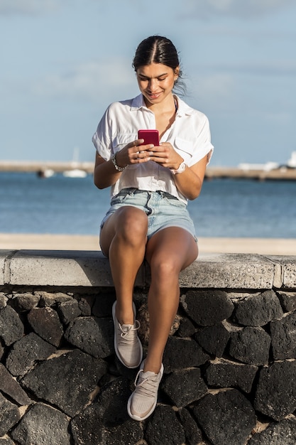 Uśmiechnięta kobieta wiadomości na telefonie komórkowym nad brzegiem morza