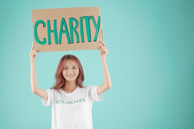 Uśmiechnięta ładna młoda wolontariuszka trzymająca nad głową papierowy znak charytatywny