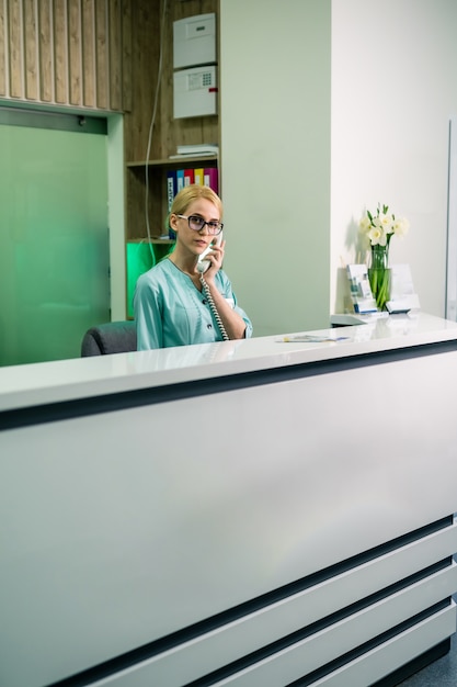 Zdjęcie uśmiechnięta lekarka trzymająca odbiornik i odbieranie połączeń telefonicznych, usługi medyczne. recepcja.