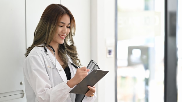 Uśmiechnięta lekarka w białym mundurze ze stetoskopem czytająca jej wykres pacjenta