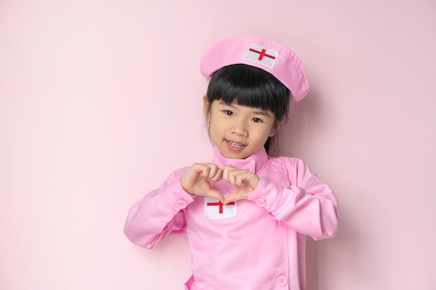 Uśmiechnięta mała azjatycka dziewczyna w mundurze medycznym Opieka zdrowotna i koncepcja medyczna na białym tle na różowym tle