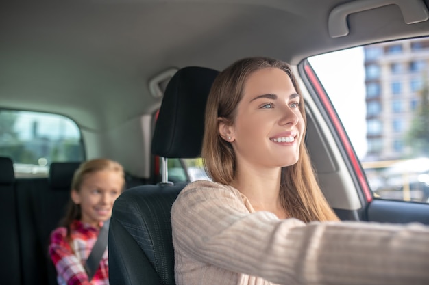 Uśmiechnięta Mama Jazdy Z Córką Siedzącą Na Tylnym Siedzeniu Samochodu