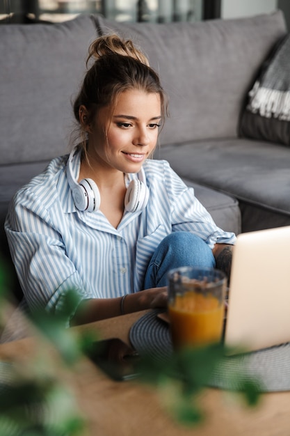 Uśmiechnięta Miła Kobieta Ze Słuchawkami Korzystająca Z Laptopa Siedząc Na Podłodze W Salonie