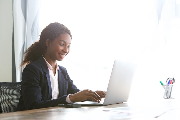 Uśmiechnięta młoda afroamerykańska bizneswoman pracująca na laptopie w biurze