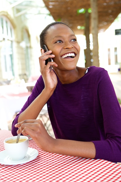Uśmiechnięta młoda afrykańska kobieta przy kawiarnią robi rozmowie telefonicza