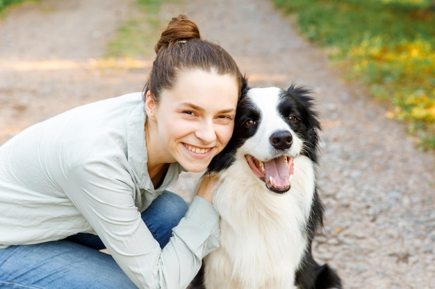 Uśmiechnięta Młoda Atrakcyjna Kobieta Bawi Się ładny Szczeniak Rasy Border Collie Na Letnim Tle Zewnątrz. Dziewczyna Trzyma Obejmując Przytulanie Przyjaciela Psa. Koncepcja Opieki Nad Zwierzętami I Zwierzętami.