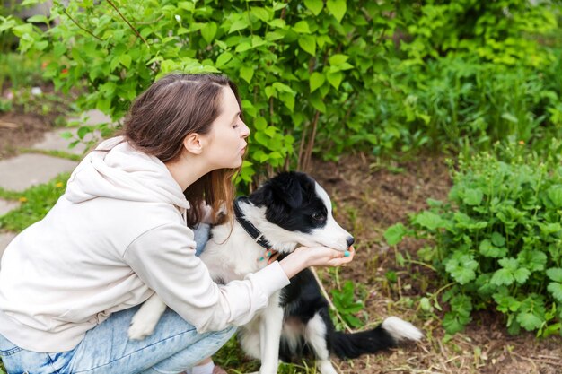 Uśmiechnięta młoda atrakcyjna kobieta obejmująca przytulającego słodkiego szczeniaka rasy border collie w letnim parku miejskim na zewnątrz w tle