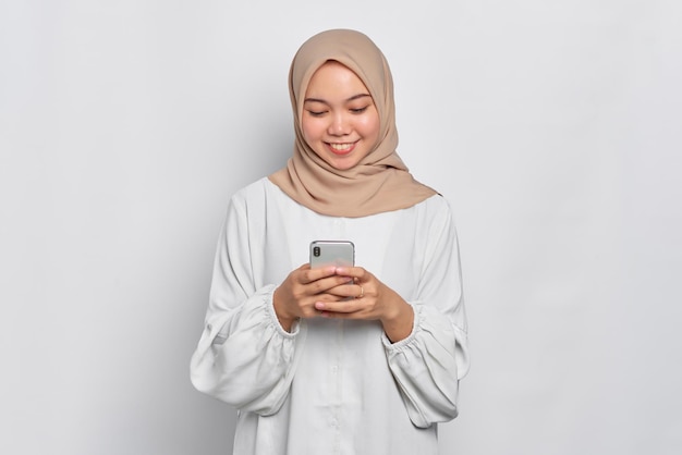 Uśmiechnięta młoda azjatycka muzułmanka korzystająca z telefonu komórkowego otrzymała dobre wieści odizolowane na białym tle