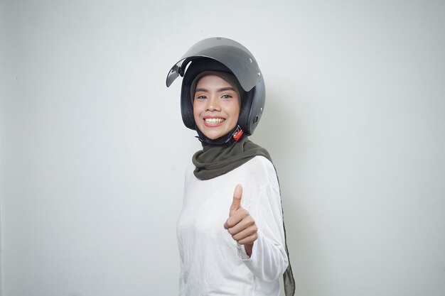 Uśmiechnięta młoda azjatycka muzułmanka pokazująca aprobaty za pomocą kasku motocyklowego