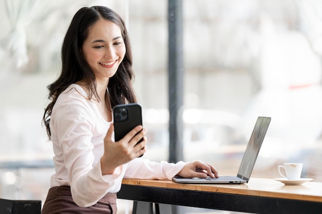 Uśmiechnięta młoda bizneswoman za pomocą smartfona siedzącego w domowym biurze