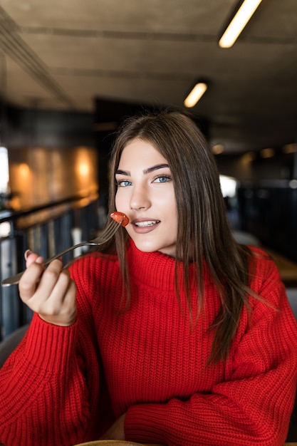 Uśmiechnięta młoda kobieta je świeżą sałatkę w restauracji