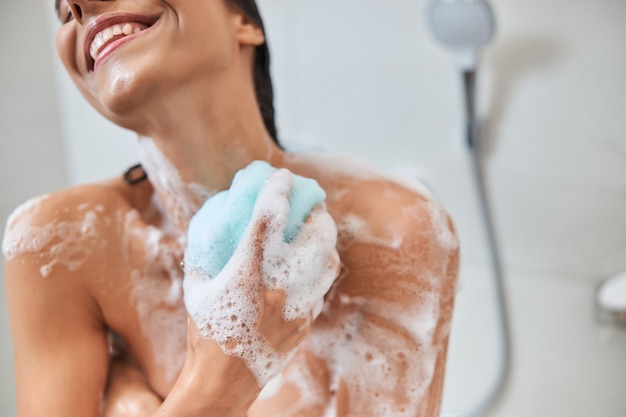 Uśmiechnięta młoda kobieta korzystająca z kąpieli loofah podczas brania prysznica