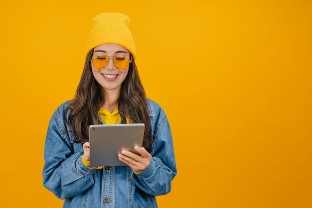 Uśmiechnięta młoda kobieta korzystająca z komputera typu tablet na żółtym tle