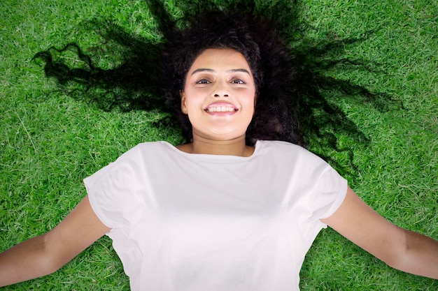 Uśmiechnięta młoda kobieta leżąc na zielonej trawie