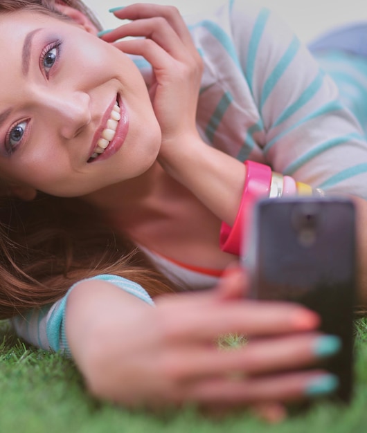 Zdjęcie uśmiechnięta młoda kobieta leżąca na trawie i robiąca selfie