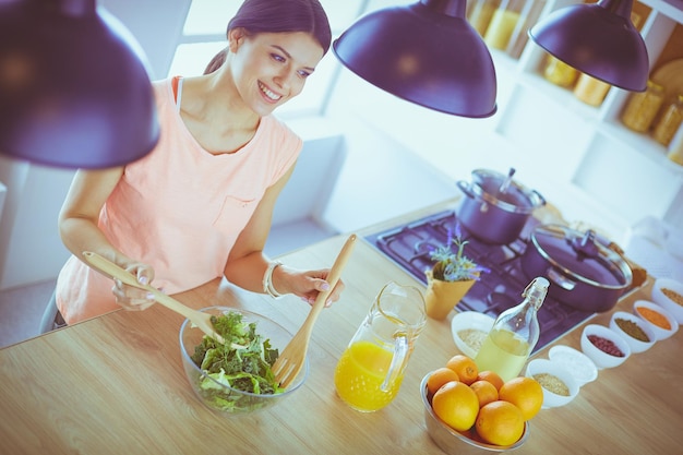 Uśmiechnięta młoda kobieta miesza świeżą sałatkę w kuchni