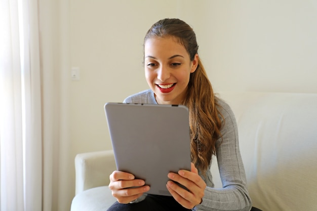 Uśmiechnięta Młoda Kobieta, Patrząc Na Komputerze Typu Tablet, Siedząc W Domu