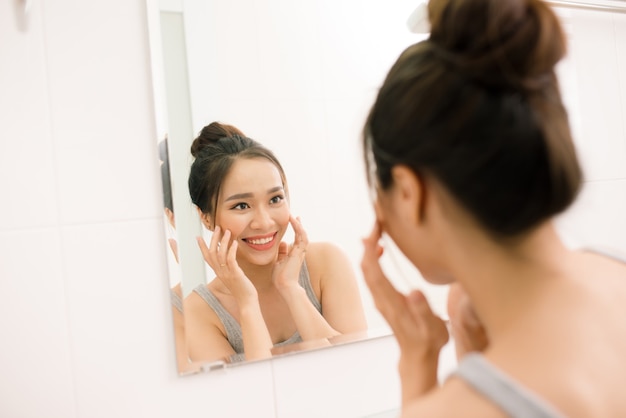 Uśmiechnięta młoda kobieta patrząca na lustro w domowej łazience